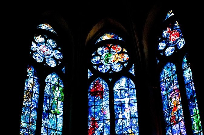 Three stained-glass windows in deep blues and reds against a dark interior