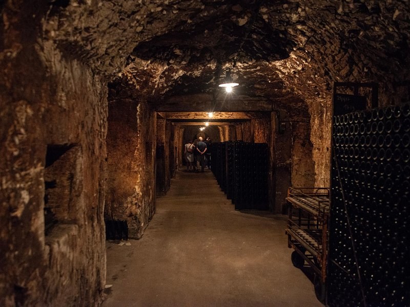 A long chalk gallery under a single lamp, bottle stacks along its walls