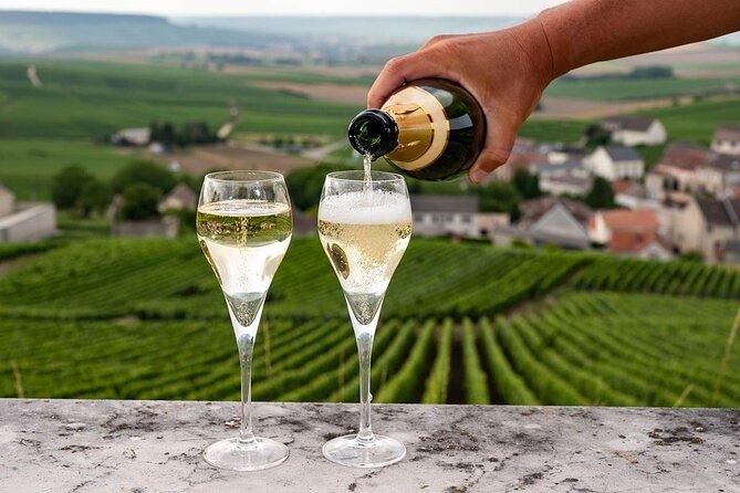 Champagne poured into two flutes on a ledge above a vineyard and a village
