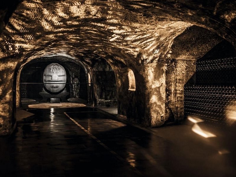 A great cask at the end of a chalk cellar, bottles stacked in the side bays