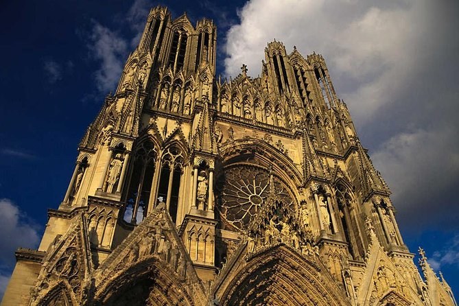 The carved west front of Reims Cathedral lit gold against a dark evening sky