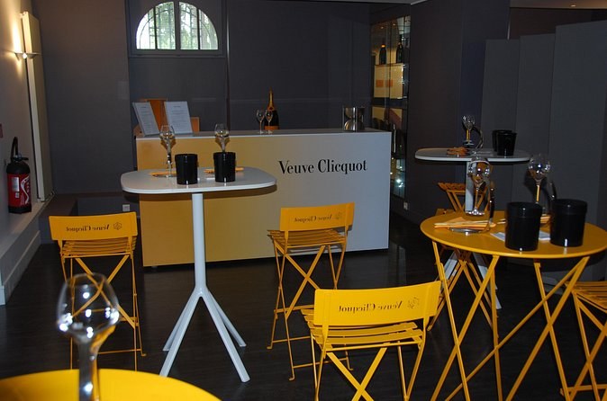 A tasting room with yellow folding chairs, high tables and the Veuve Clicquot name on the counter